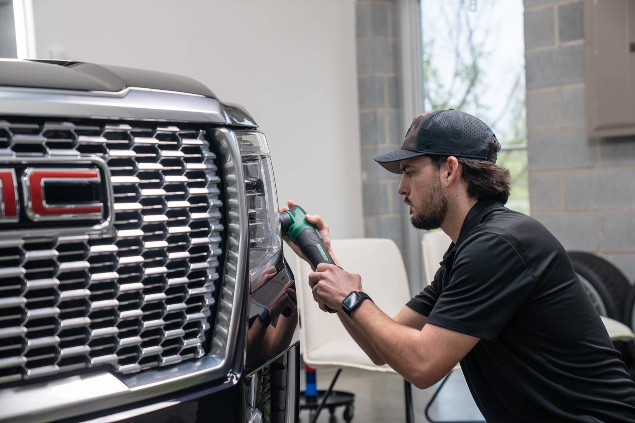 Auto detailing specialist polishing the front grille and headlight of a dark GMC vehicle to correct paint imperfections.