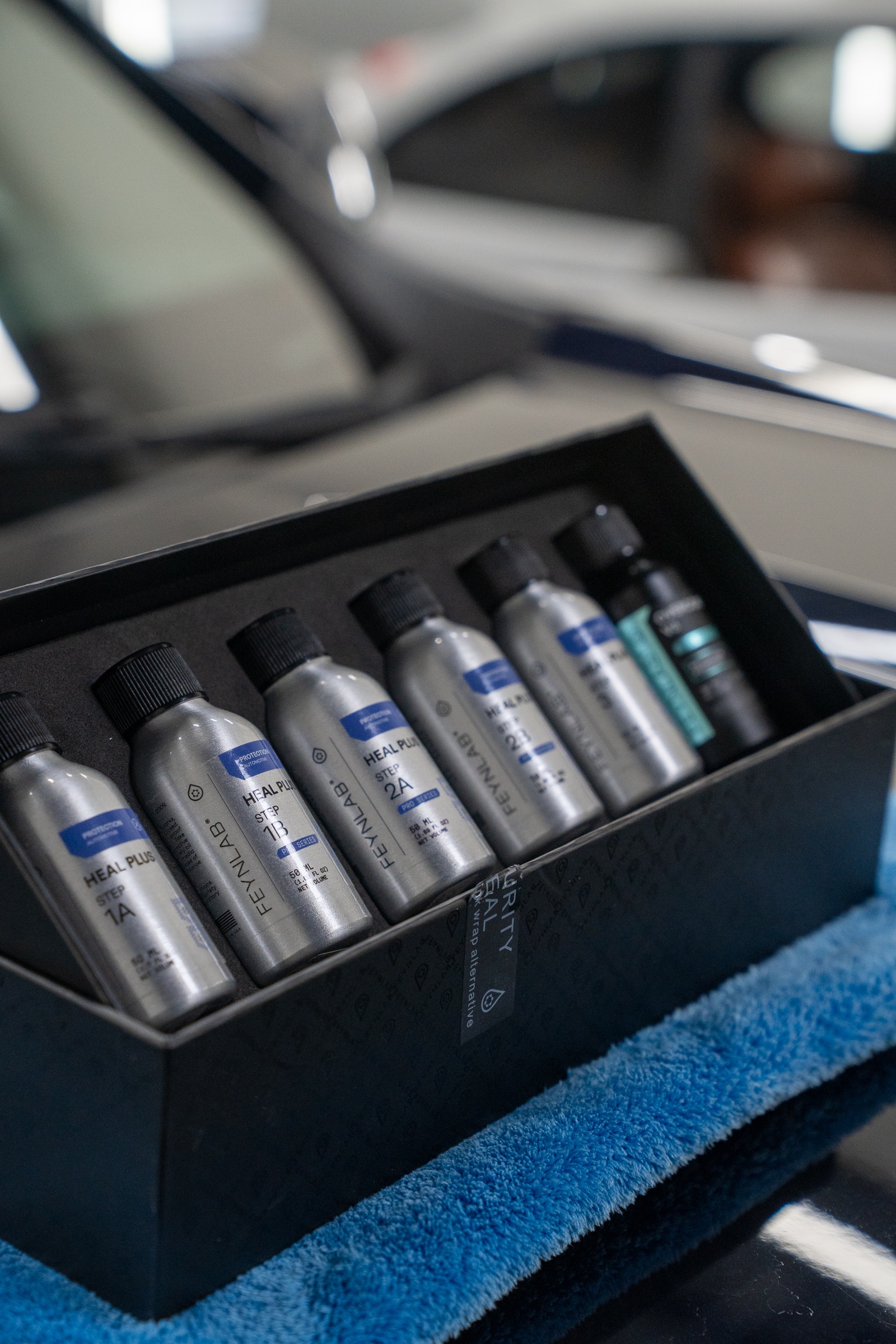A premium display box of Feynlab Heal Plus self-healing ceramic coating bottles resting on a blue microfiber towel at Ghostwerkz.
